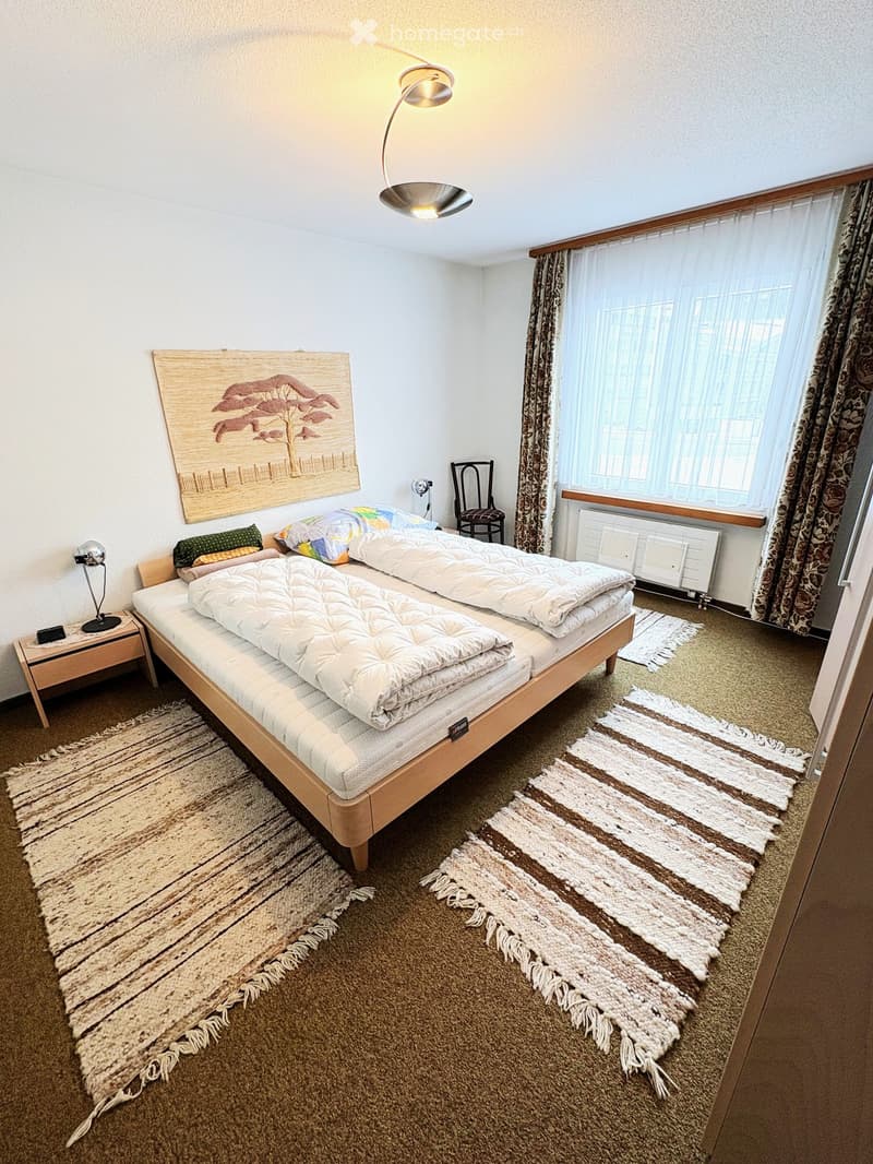 Cozy bedroom with two single beds, nightstand, chair, and decorative rugs.