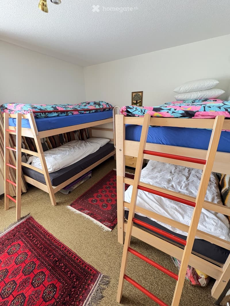 Cozy bedroom with two wooden bunk beds, colorful bedding, and red patterned rugs on the floor.