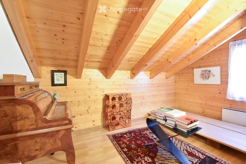 Cozy attic room with wooden walls and ceiling, featuring a sofa, a small table with books, a framed picture, and a decorative cabinet.
