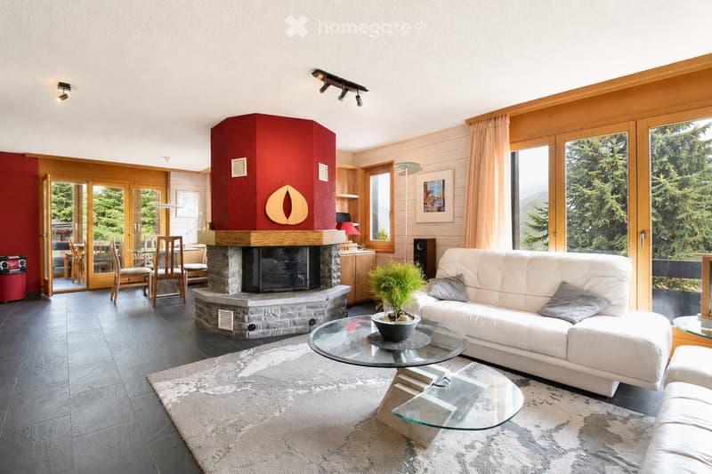 Modern living room with a white leather sofa, glass coffee table, fireplace, large windows with scenic mountain view, and dining area visible through an open doorway.