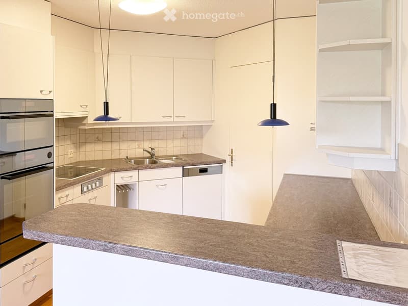 Modern kitchen with white cabinets, granite countertops, stainless steel appliances, and pendant lights.