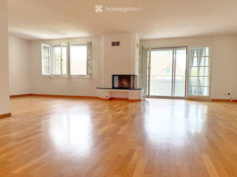 Empty room with wooden flooring, large windows, and a fireplace niche.