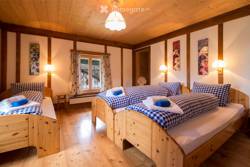 Cozy wooden bedroom with two single beds, checkered bedding, wooden floor, and warm lighting.