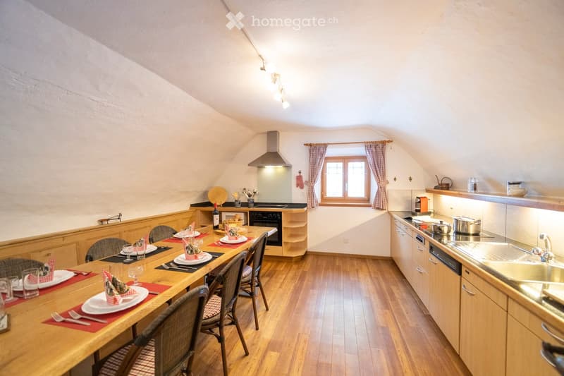 Cozy attic kitchen with wooden dining table, chairs, oven, stove, sink, and cabinets.