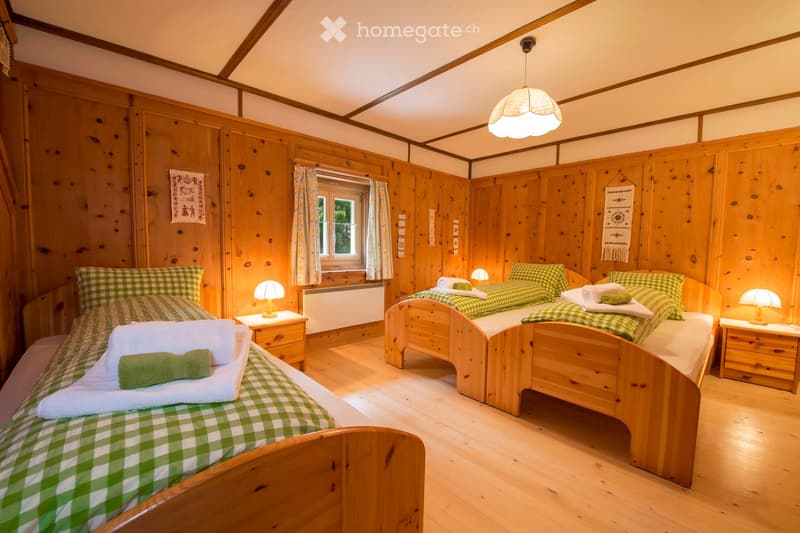 Cozy wooden bedroom with two single beds, green checkered bedding, nightstands, lamps, and towels.