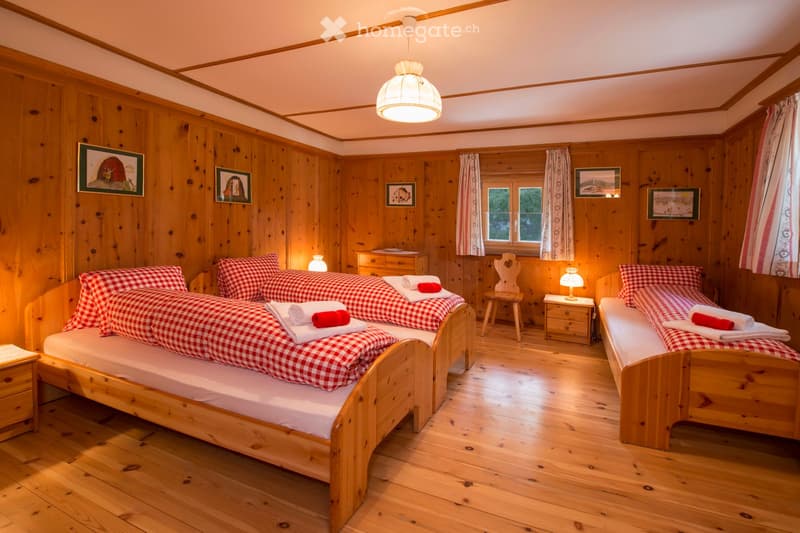 Cozy wooden bedroom with two single beds, nightstands, a wooden chair, and framed pictures on the walls.