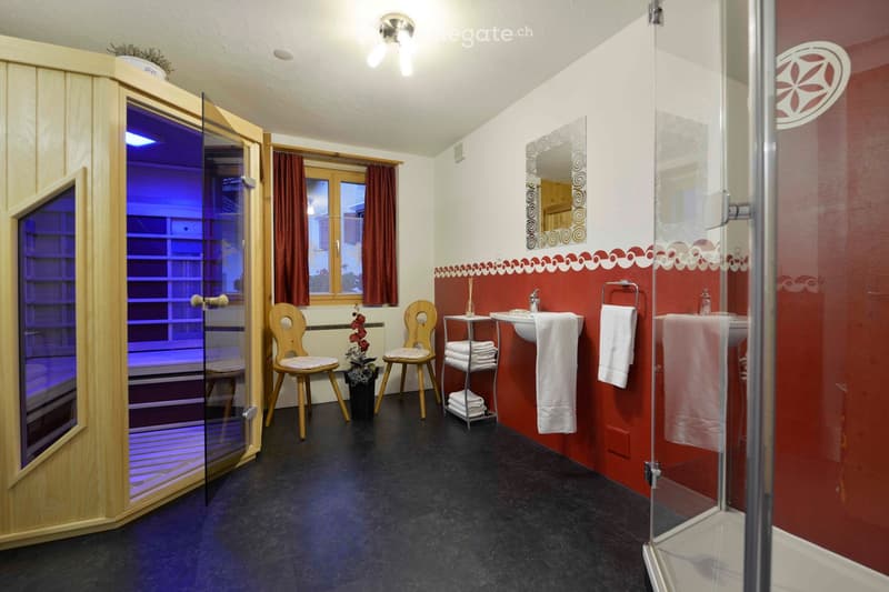 Bathroom with red and white decor, featuring a sink, mirror, towel, two wooden chairs, a small table with a plant, and a glass-enclosed shower area.