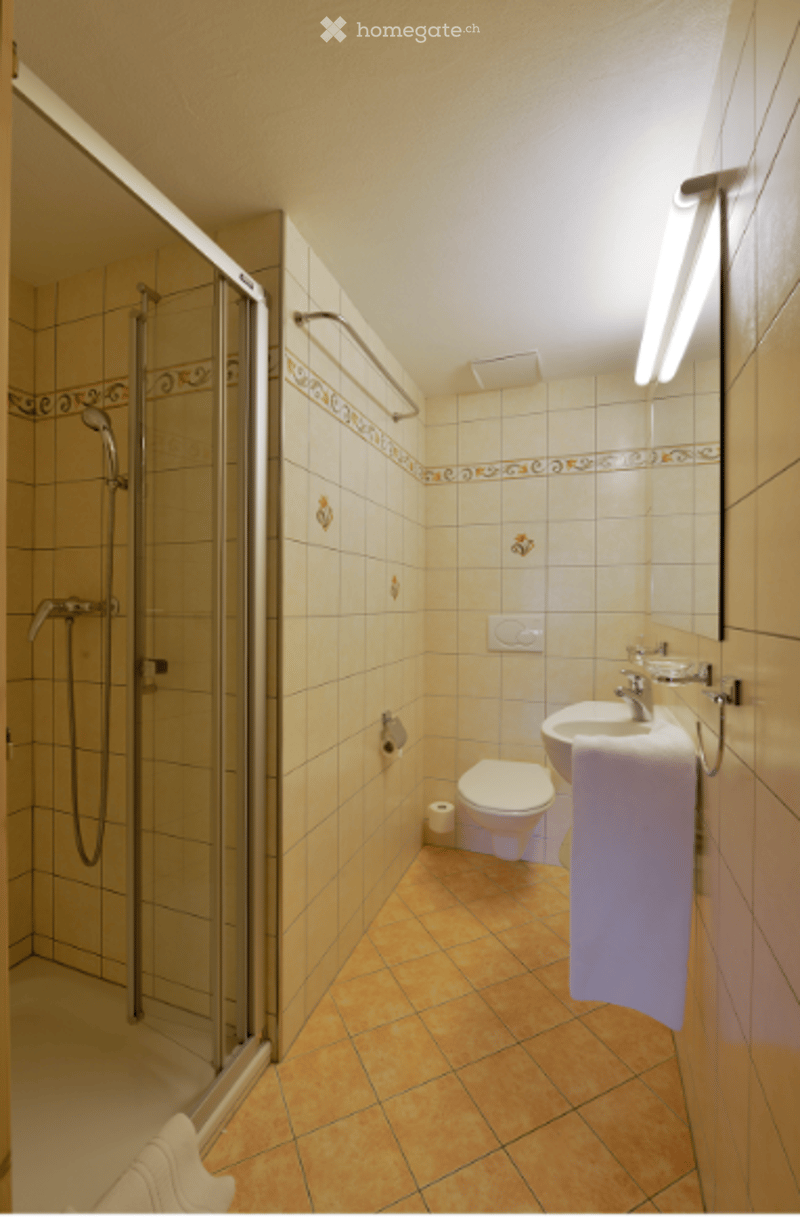 Modern bathroom with tiled walls and floor, featuring a shower stall, toilet, sink, and mirror. A towel hangs on the side.
