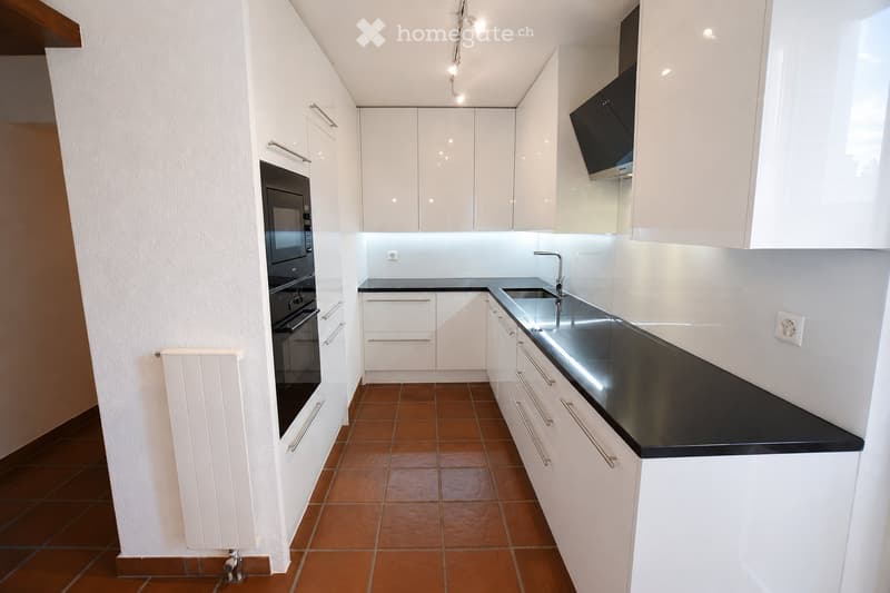 Modern kitchen with white cabinets, black countertops, and stainless steel appliances, including an oven and microwave. The floor is tiled in a warm terracotta color.