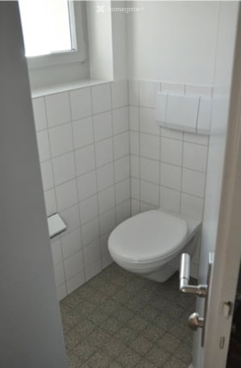Small bathroom with white tiled walls, a toilet, and a door.