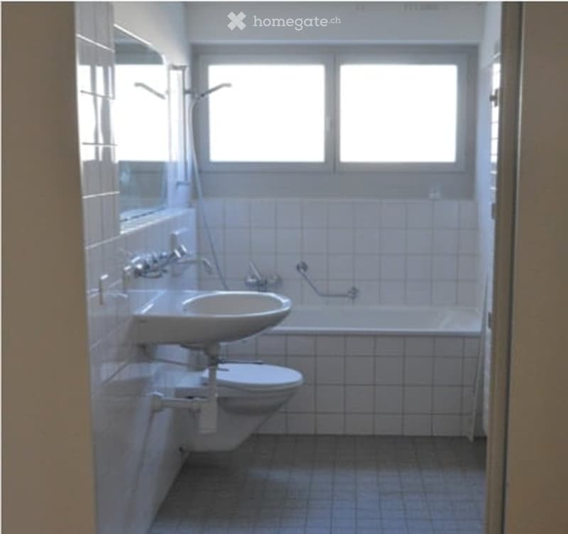 Modern bathroom with white tiles, a sink, toilet, bathtub, and a large window for natural light.