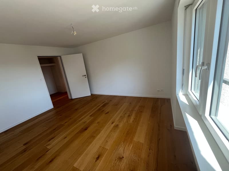 Empty room with wooden flooring, white walls, and a large window with a white sill. An open closet door is visible on the left side.