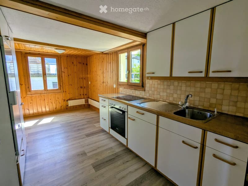 Bright kitchen with white cabinets, wooden countertops, and a sink. The space features wooden walls and flooring, with large windows allowing natural light to fill the room.