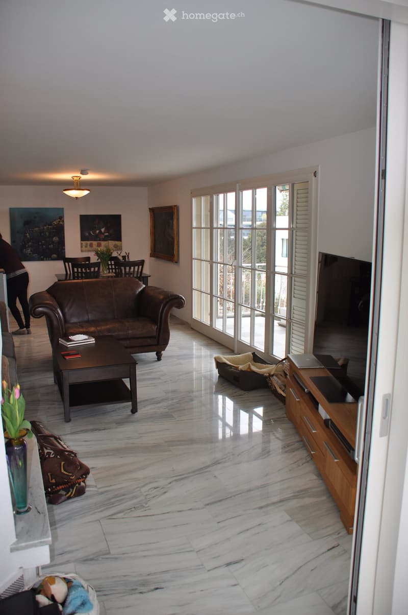 Spacious living room with marble flooring, large windows, leather sofa, coffee table, dining area, TV stand, and decorative items.