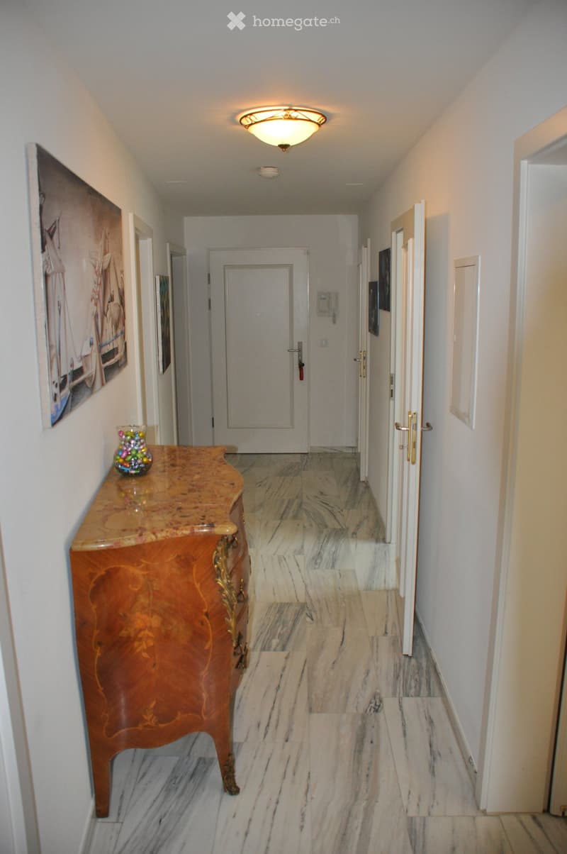 Elegant hallway with marble flooring, a wooden table with a decorative vase, and several doors leading to other rooms.