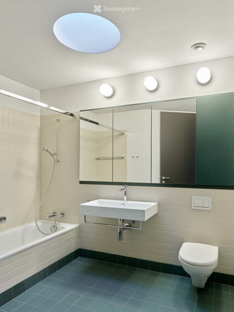 modern bathroom with white bathtub, white sink, white toilet, green tiles, large mirror, round ceiling light