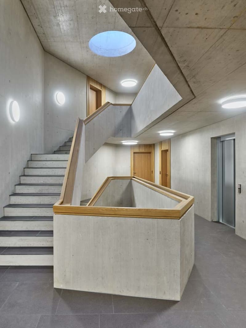 Concrete walls, concrete floor, staircase, elevator, wooden handrail, circular ceiling lights