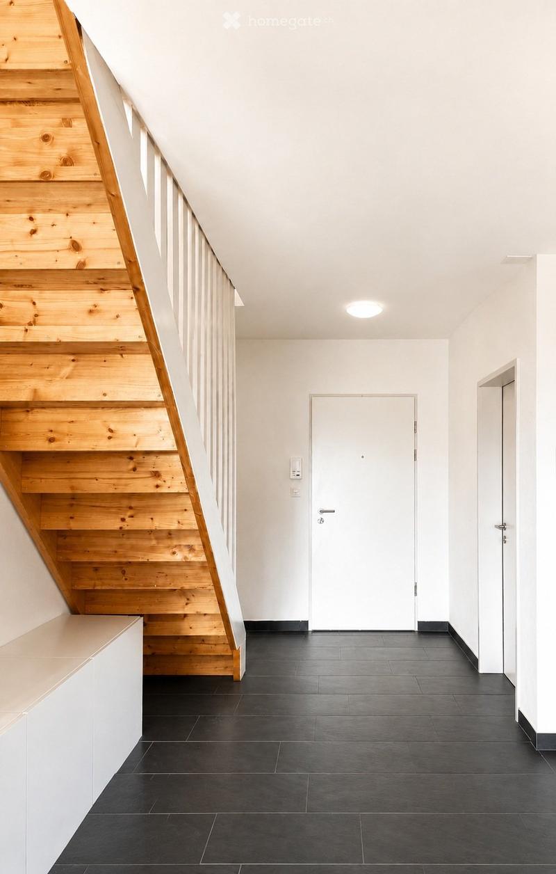 Modern hallway with wooden staircase, black tiled floor, white walls, and recessed lighting.