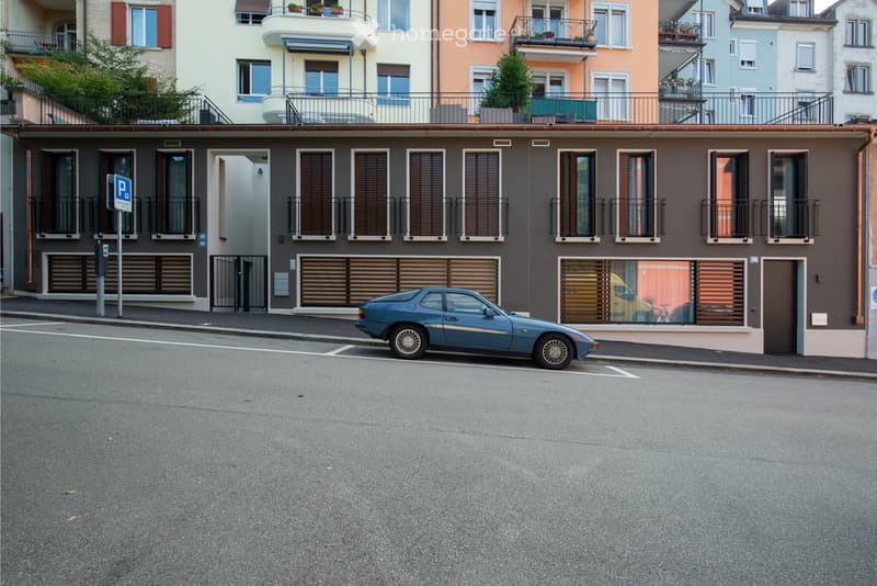 3 story building, brown color, multiple balconies, blue car parked in front, street sign