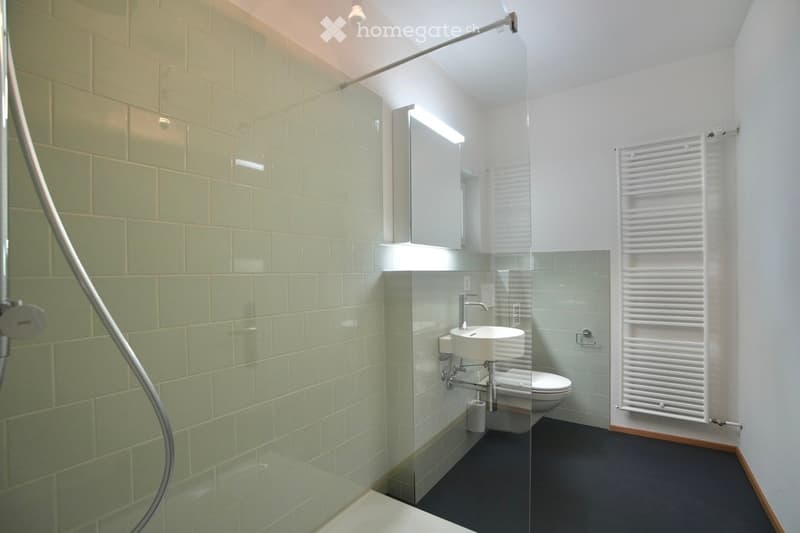 Modern bathroom with green tiled walls, white fixtures, a glass-enclosed shower area, and a white radiator.