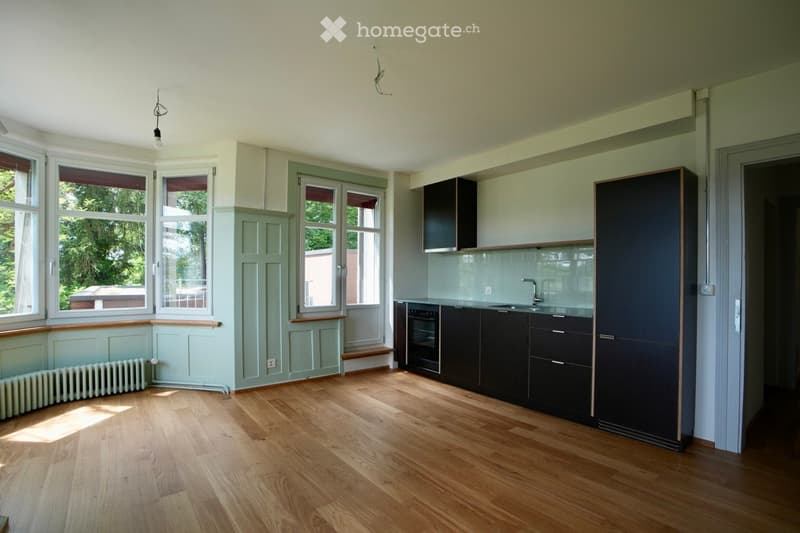 Bright, modern kitchen with wooden flooring, large windows, and dark cabinets. Features include a sink, faucet, and oven.