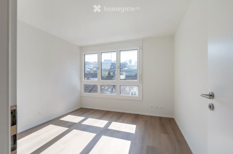 Empty room with white walls, wooden floor, and a large window. No furniture or equipment.