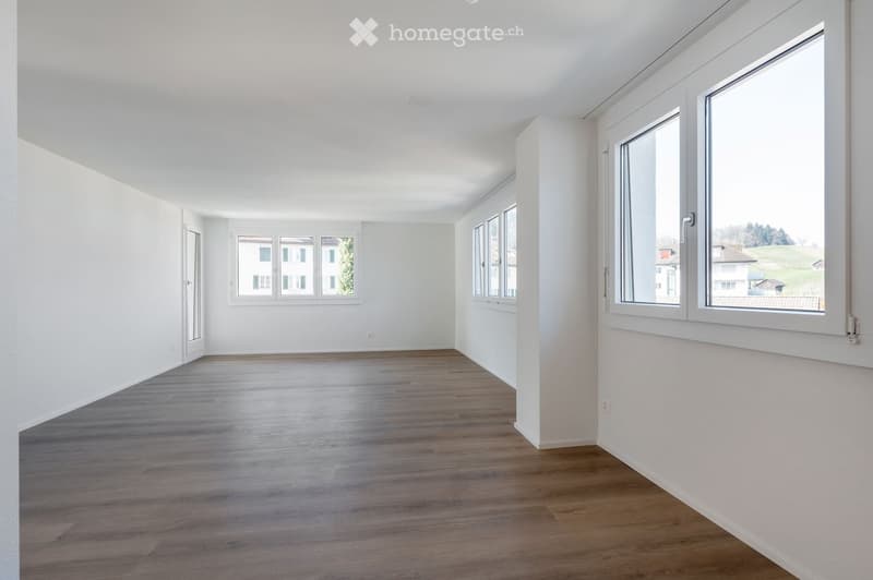 Completely empty room with white walls, wooden floor, and large windows. No furniture or equipment.