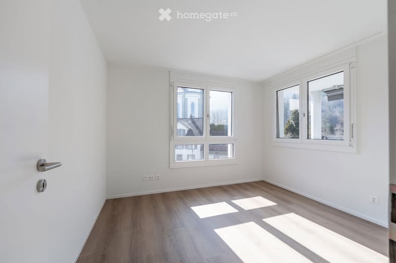 Empty room with white walls, wooden floor, and two large windows. No furniture or equipment.
