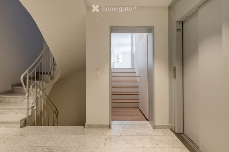 A modern hallway with marble flooring, a spiral staircase, and an open door leading to a staircase.