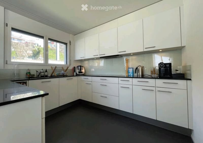 Modern kitchen with white cabinets, black countertops, and stainless steel appliances. Features include a sink, coffee maker, and various kitchen items on the counter.