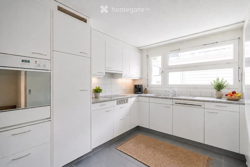 Modern kitchen with white cabinets, stainless steel appliances, granite countertops, and a small woven rug on the floor.