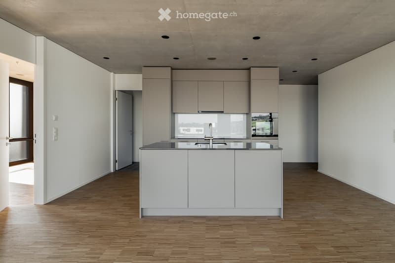 Modern, minimalist kitchen with white cabinets, a central island, and a sleek sink. The space features light wooden flooring and ample natural light from large windows.