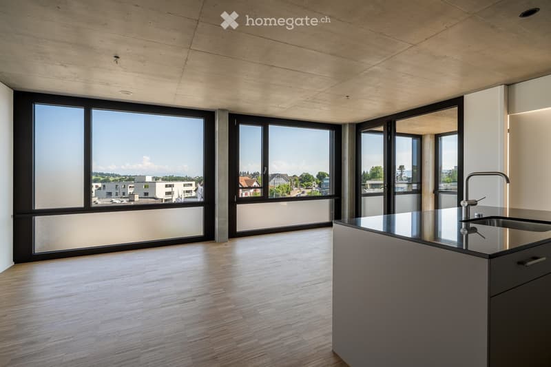 Modern kitchen with light wooden flooring, large windows, and a sleek black countertop with a built-in sink and faucet.