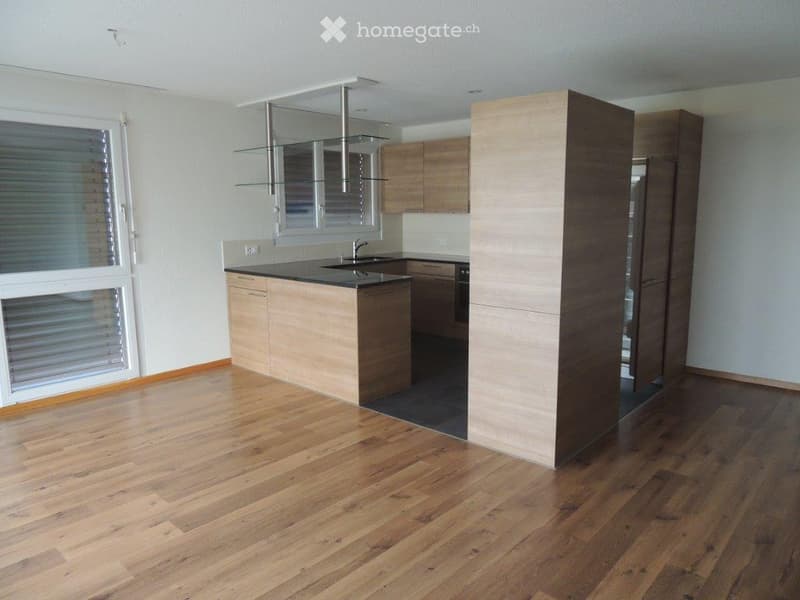 Modern kitchen with light wooden cabinets, black countertop, and a central island. Features a stainless steel sink and faucet, with a large window providing natural light.