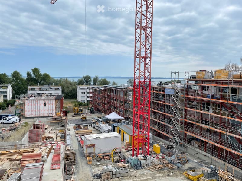 A multi-story residential building under construction with scaffolding, cranes, and construction materials scattered around the site.