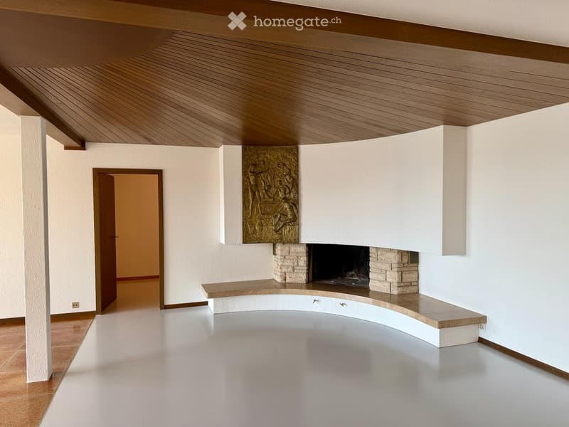 Modern living room with a central fireplace, sculptural artwork above it, and a curved wooden bench seating area.