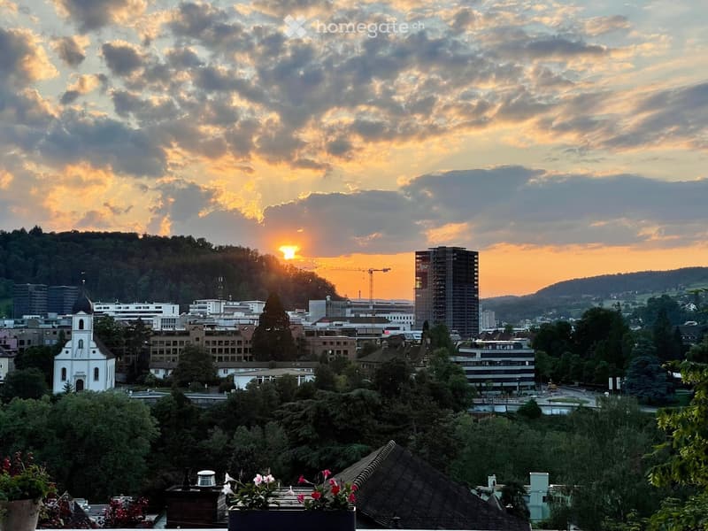 Panoramic cityscape view at sunset, featuring a mix of modern high-rise buildings, historic structures, and lush greenery.