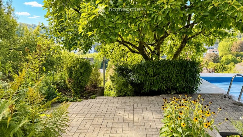 Well-maintained garden with a swimming pool, lush greenery, and a brick patio.