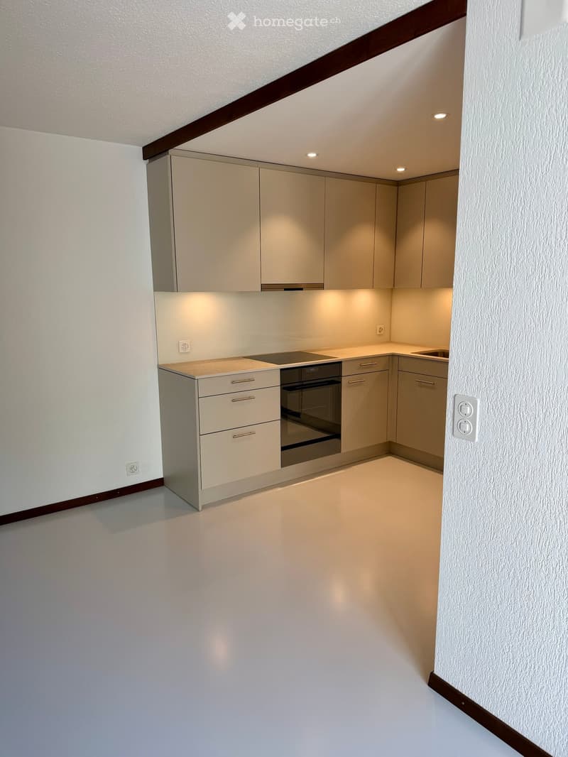 Modern kitchen with light-colored cabinets, an oven, and a sink, featuring sleek countertops and built-in lighting.