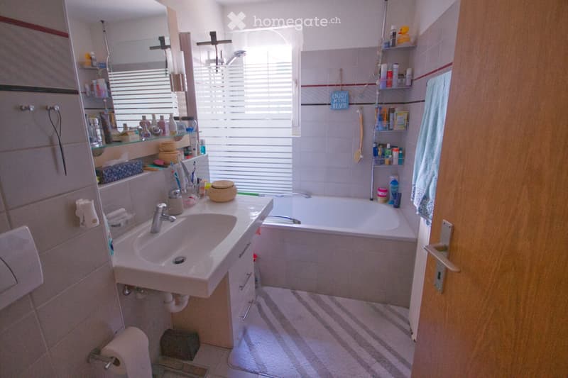 Bathroom with a sink, bathtub, mirror, and various toiletries. The space includes a towel, a bathroom cabinet, and a shower shelf with toiletries.