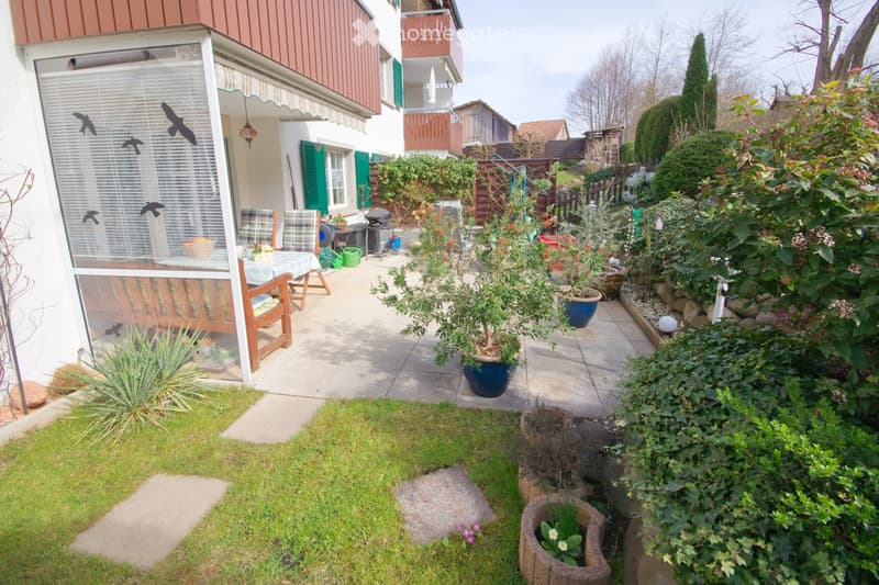 Garden with patio seating, potted plants, small water feature, and lawn area.