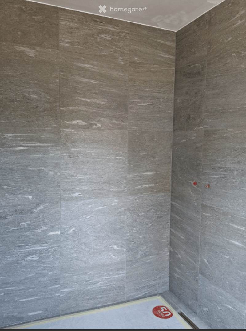 Empty room with grey stone-textured walls and a grey floor, showing a small red sticker on the floor.