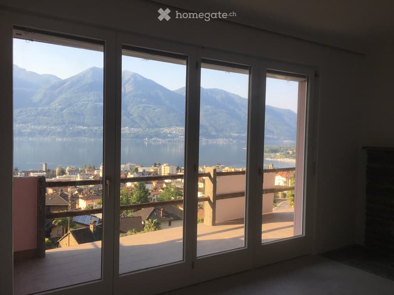 Large balcony with expansive view of a lake and surrounding mountains, accessible through large glass doors.