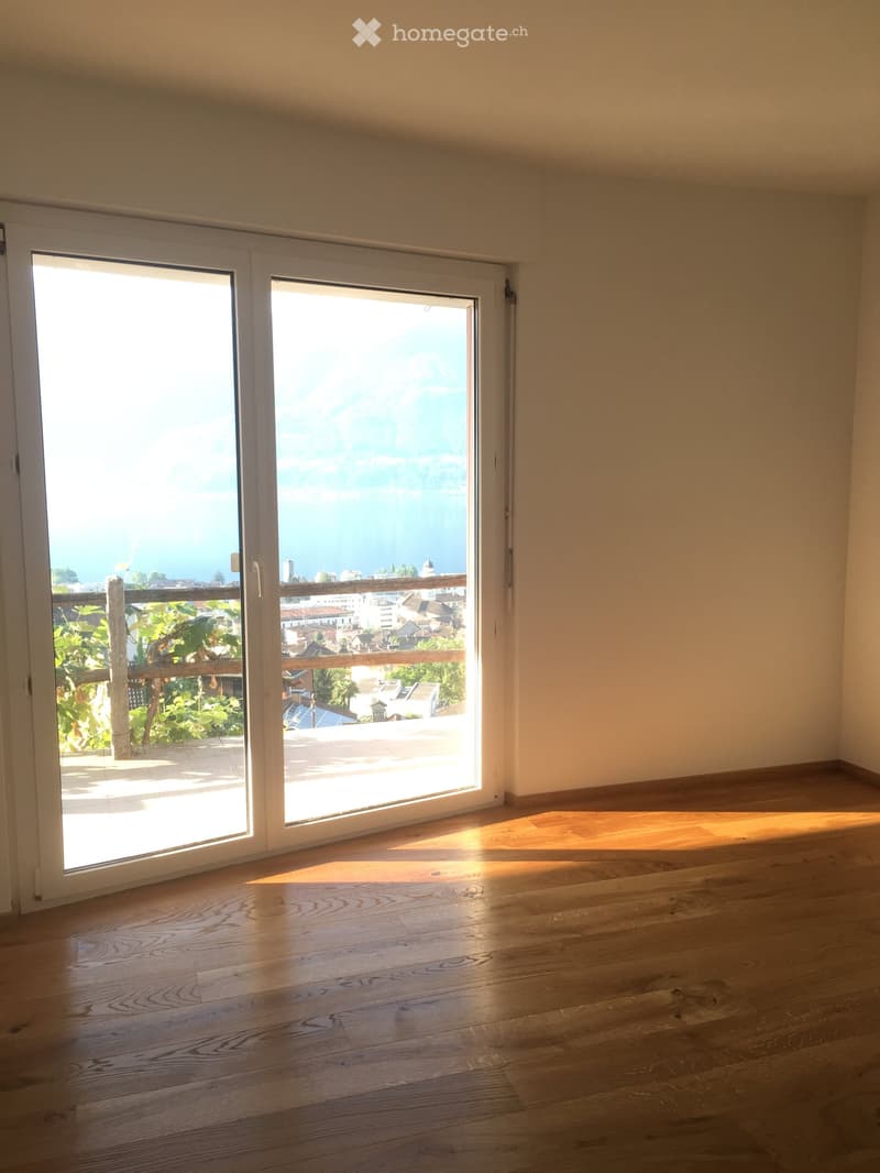 Empty room with wooden flooring and large sliding glass doors leading to a balcony with a scenic view of the city and sea.