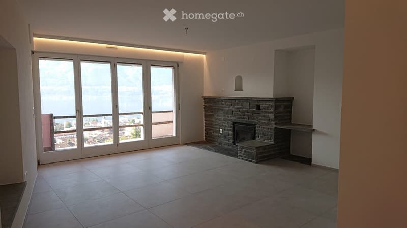 Empty room with tiled floor, stone fireplace, large sliding glass doors leading to a balcony with a scenic view.