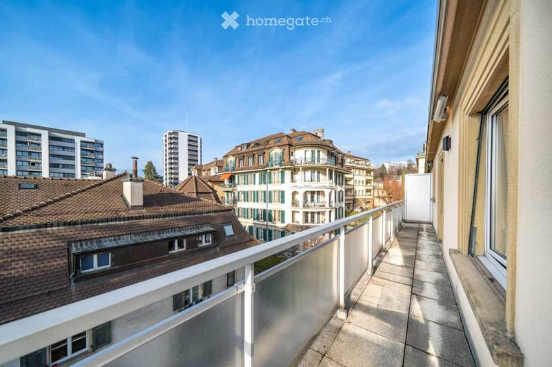 Balcony with a white railing, overlooking a cityscape with various buildings and rooftops.