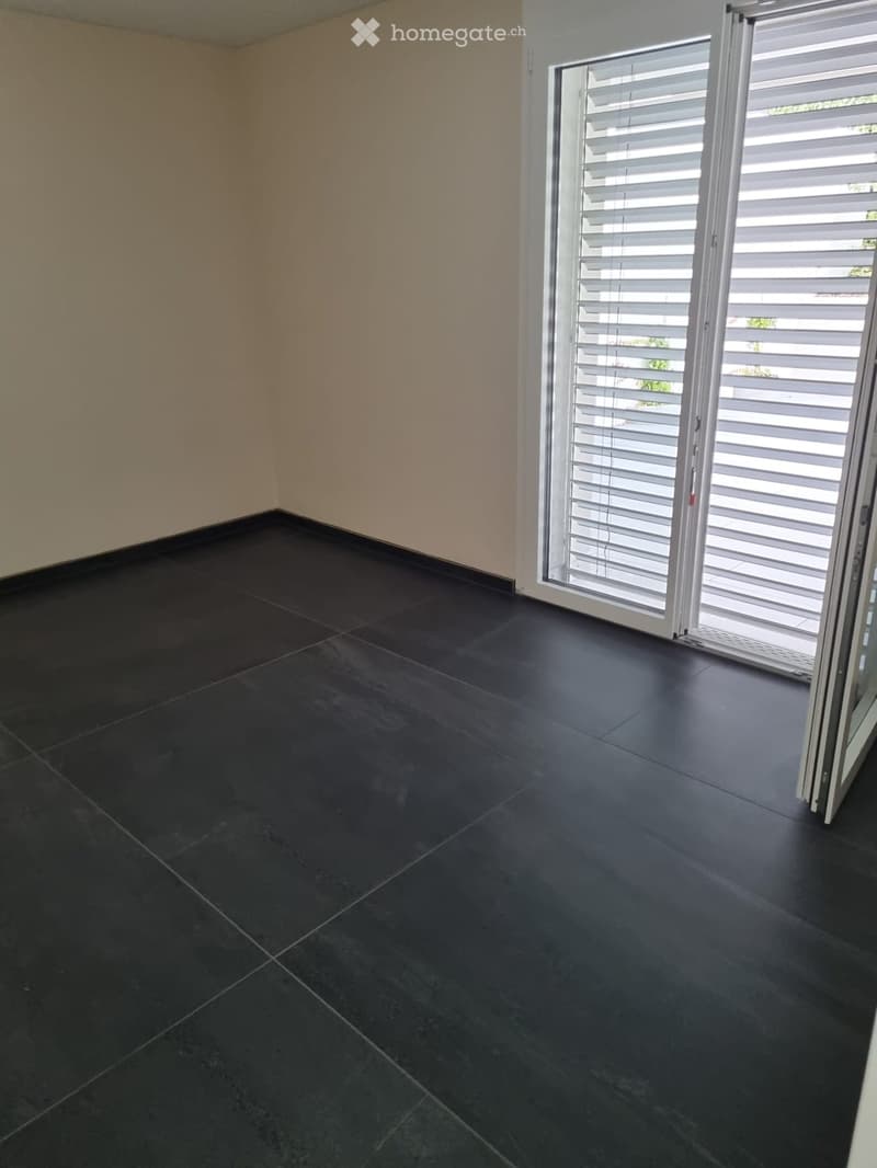 Empty room with dark tiled flooring and light-colored walls, featuring a large sliding glass door with blinds.