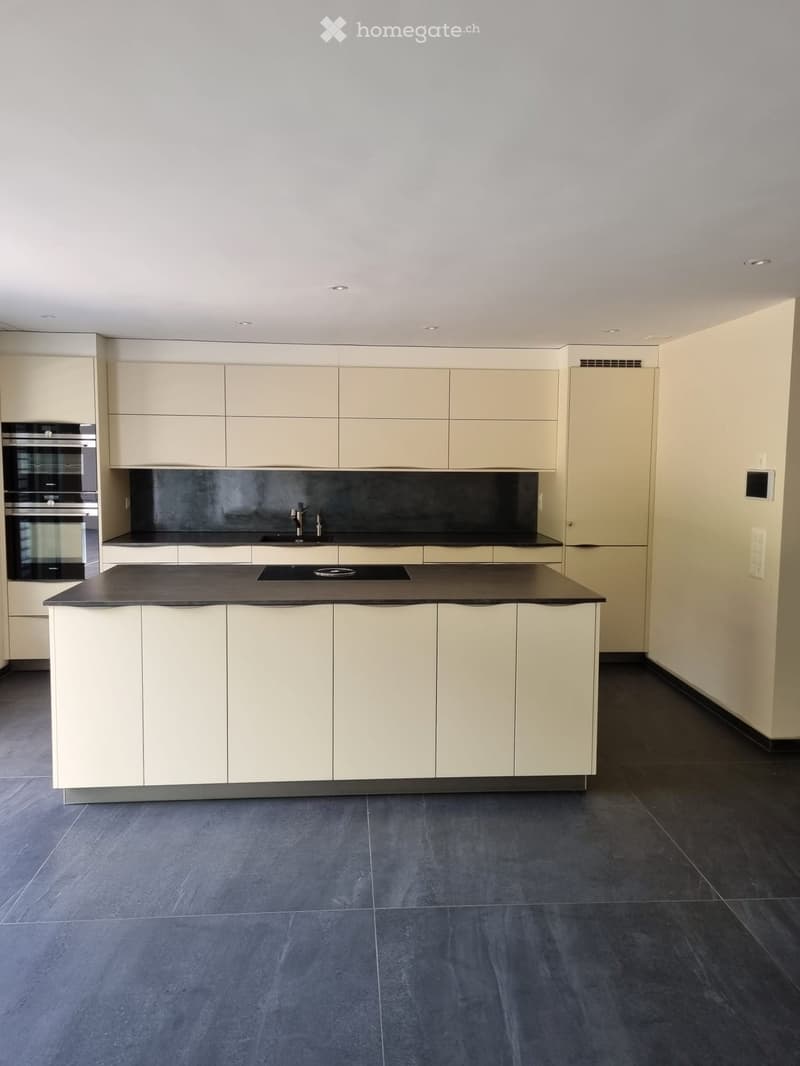 Modern kitchen with light-colored cabinets, a central island, and built-in appliances including an oven and sink.