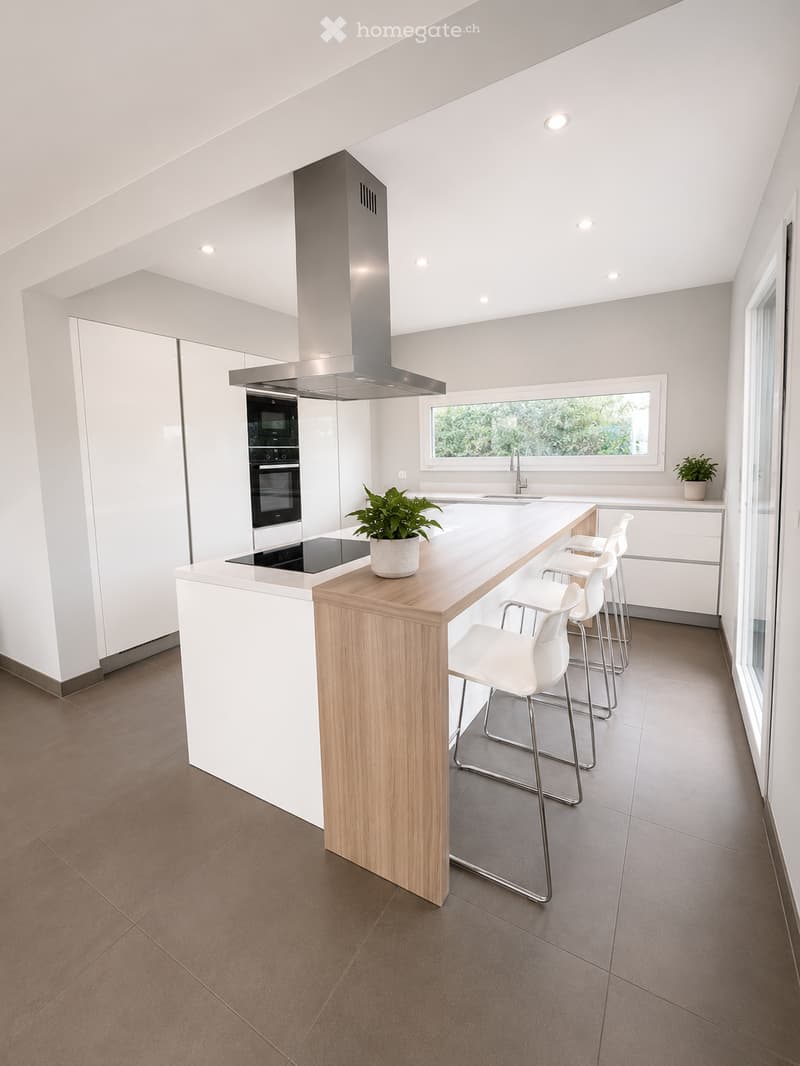 Modern kitchen with white cabinets, a wooden island, four white stools, an oven, a range hood, a sink, and a potted plant on the island.