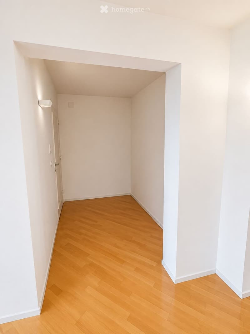 Empty room with light wooden flooring and white walls, featuring a doorway leading to another space.